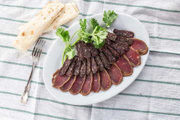 Dried meat basturma beef jerky with parsley on white plate and lavash bread on striped tablecloth