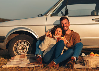 Beautiful young couple enjoying picnic time on the sunset. They drinking tea and sitting in a...