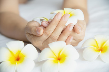 Obraz na płótnie Canvas Lady hand holding beautiful white yellow plumeria flowers on white bed - people with spa flower peaceful mind concept