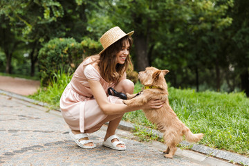 Portrait of nice woman stroking dog and smiling while squatting in summer park