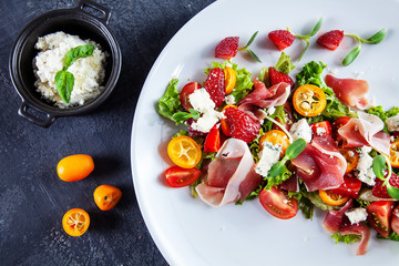 Close up view on fresh, summer salad with cherry tomato, strawberry, jamon and microgreen. Tasty food flat lay. Food for healthy and delicious lunch. Copy space. Top view