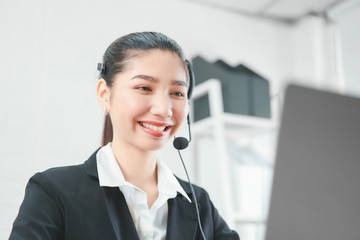 Smiling Asian woman consultant wearing microphone headset of customer support phone operator at...