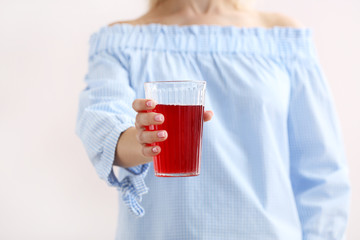 Woman holding glass of tasty pomegranate juice on light background, closeup