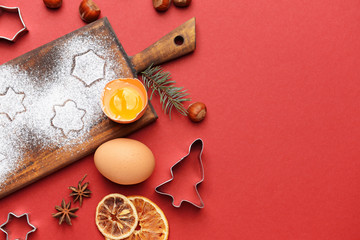Wooden board with cookie cutters and ingredients on color background