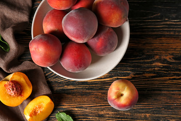 Bowl with tasty peaches on wooden table