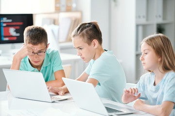 Fototapeta na wymiar Cute schoolchildren sitting by desk in classroom while browsing in the net