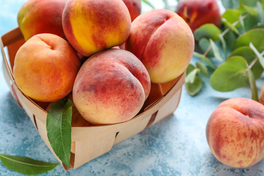 Box with tasty peaches on color background