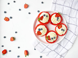 Cupcakes with cream cheese, strawberry and blueberry on white texture and on trendy kitchen towel.