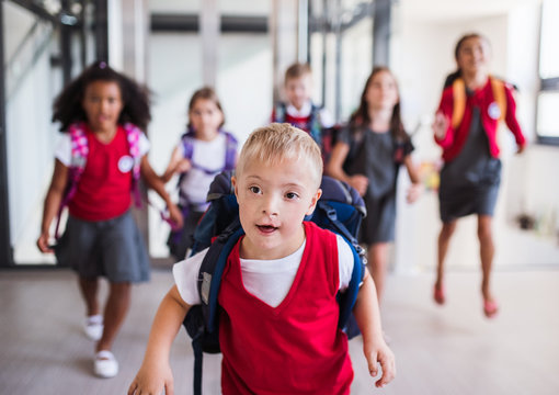 A Down-syndrome School Boy With Group Of Children In Corridor, Running.