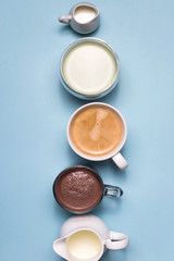 Coffee, cocoa and matcha with white creamers of milk on blue