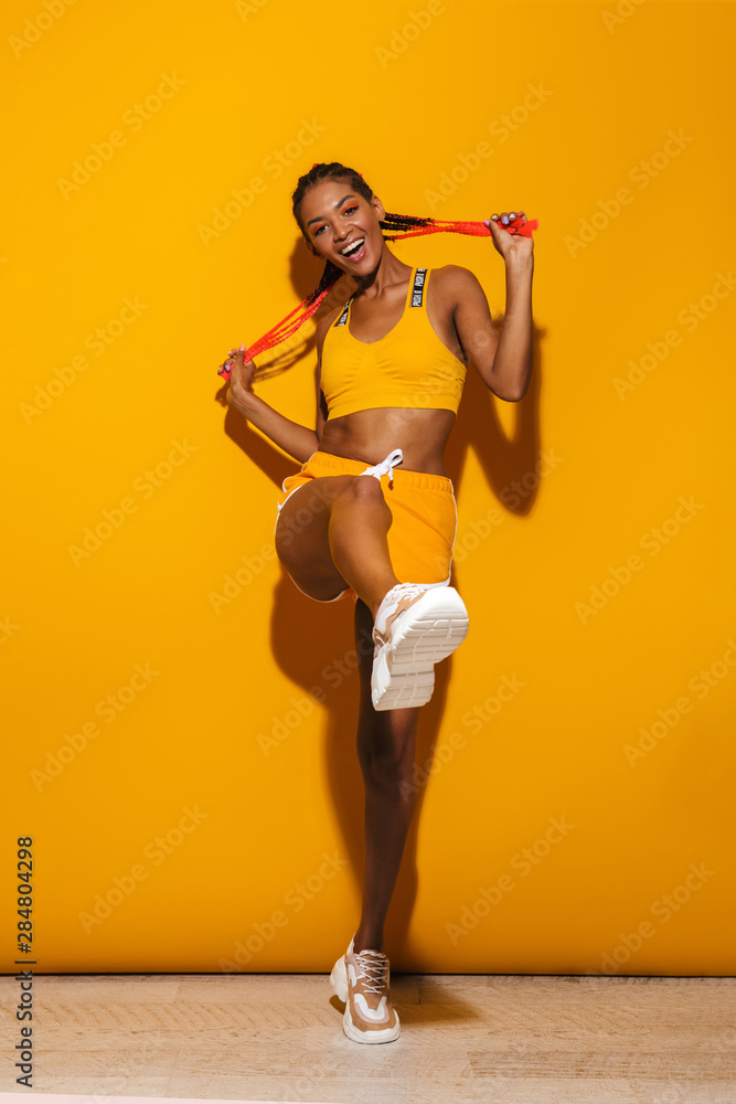 Wall mural Image of beautiful african american woman dressed in tracksuit dancing and smiling at camera - Wall murals