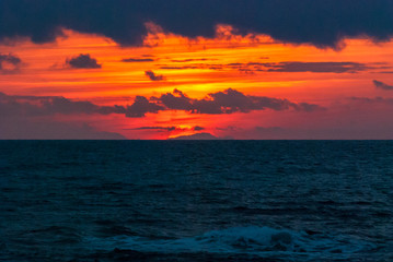 Gli ultimi raggi del sole che tramonta dietro un cielo pieno di nuvole rosse visti da Livorno