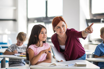 A teacher walking among small school children on the lesson, explaining.