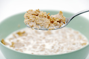 Scoop of the cereal flake with milk by stainless steel spoon from the green bowl isolated on white background