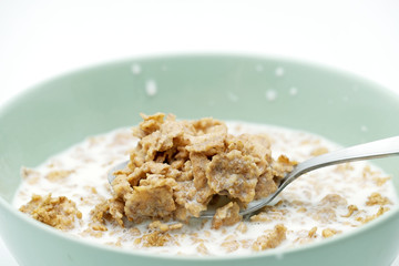 Scoop of the cereal flake with milk by stainless steel spoon from the green bowl isolated on white background