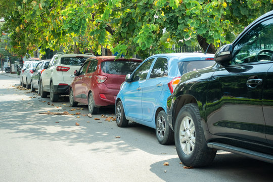 Parallel cars parking on street with green trees