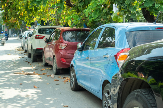 Parallel cars parking on street with green trees