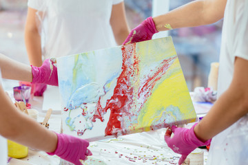 Woman painter holding hair dryer while female beginnres studying creating fluid acrylic abstract...