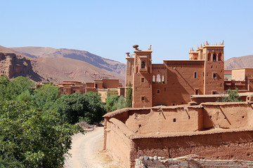 Big mud house near green trees in the dry Atlas Mountains in Morocco.