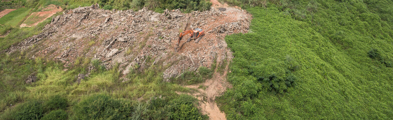 Aerial view of an orange large excavator striking a gravel while working in the field