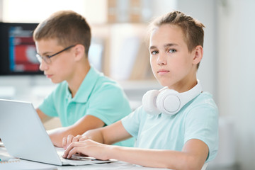 Obraz premium Cute and clever schoolboy with headpones on neck working over homework