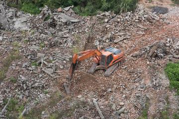 Aerial view of an orange large excavator striking a gravel while working in the field