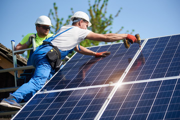 Two workers technicians installing heavy solar photo voltaic panels to high steel platform....