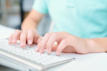 Human hands pushing keys of computer keyboard while sitting by desk
