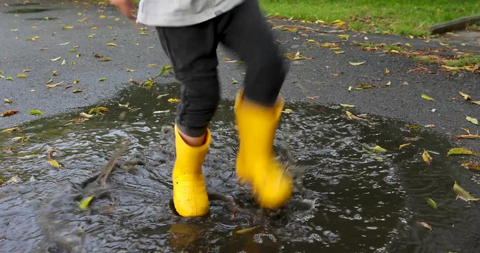 Baby boy stomping through puddles in yellow rubber boots