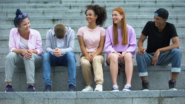 Group of multiethnic young people sitting on academy stairs, leisure time