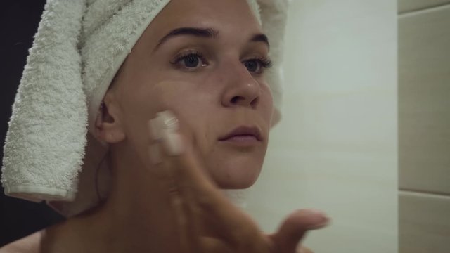 Young woman applying foundation cream after morning shower.