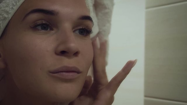 Young woman looking at mirror and touching face after morning shower.