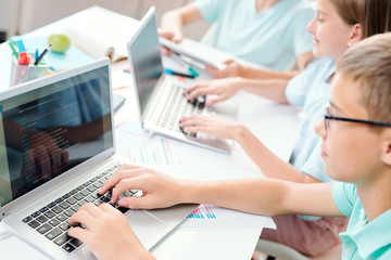 Clever learners of middle school touching keys of laptop keypad