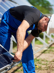 Technician working on exterior voltaic stand-alone solar panel system installation on bright sunny summer day. Renewable ecological cheap green energy production concept.