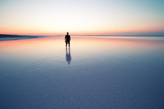 Silhouette of man departing into sunset on smooth water of lake