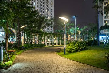 Garden walkway with lamps at night. Tree and building on background