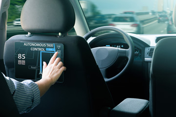 Woman passenger sitting in the backseat and selects a route when her self-driving car rides on the highway.