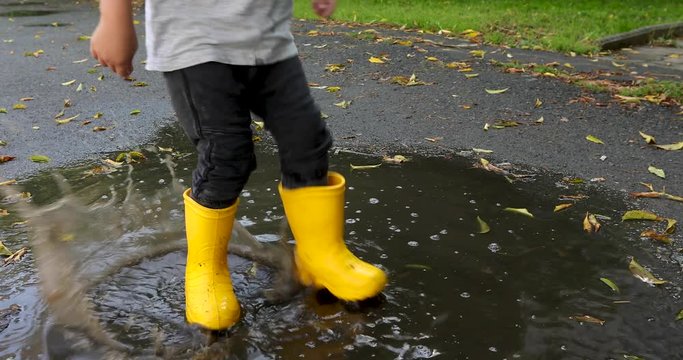 Baby boy stomping through puddles in yellow rubber boots