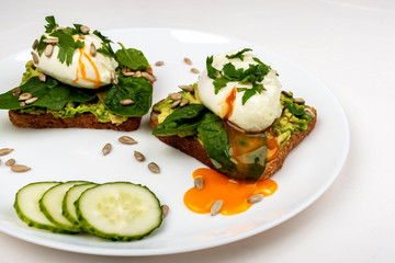 Poached eggs with avocado, spinach leaves and seeds on toasts bread on a white plate on the white background. Healthy breakfast or snack.