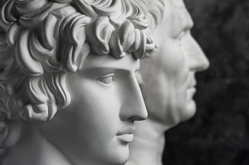 Gypsum copy of ancient statue Augustus and Antinous head on dark textured background. Plaster sculpture mans face.