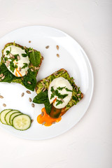 Poached eggs with avocado, spinach leaves and seeds on toasts bread on a white plate on the white background. Healthy breakfast or snack. Top view.