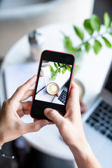 Hands of young female holding smartphone over table while photographing
