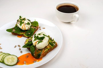 Poached eggs with avocado, spinach leaves and seeds on toasts bread on a white plate on the white background. Healthy breakfast or snack. Copy space.