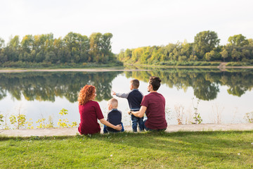 Parenthood, nature, people concept - family with two sons sitting near the lake