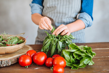 woman cooking salad with green leaves, mozzarella and tomatoes on the wooden table and wooden plate