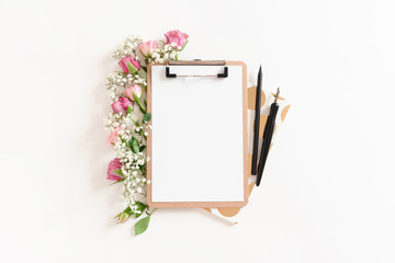 Flatlay of clipboard mockup with frame made of stationery and flowers on white background