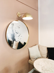 Modern Nordic Scandinavian interior design. Bright open space with pale pink wall, round gold mirror, gold lamp, marble table and comfortable couch with soft curtains. Apartment for rent concept.