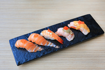 Sushi seafood set served on black stone plate on wood table. Japanese cuisine.