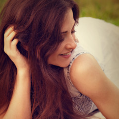 Obraz premium Beautiful smiling young woman with long hair lying on the grass on summer green background. Closeup outdoor toned color bright portrait.