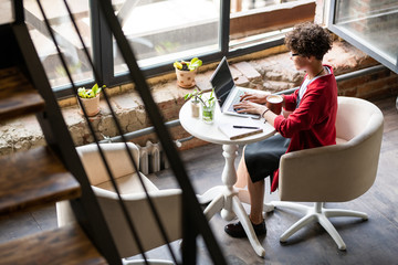 Pretty young businesswoman looking at laptop display while typing by table
